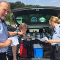 Zwei Polizisten beraten einen Mann am Autobahnrastplatz zur Ladungssicherung am Kofferraum eines Autos