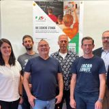 Gruppenfoto: Neun Personen stehen vor einem Info-Plakat zum Onlinepräventionstermin "DIE SICHERE STUNDE".