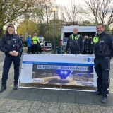 Das Bild zeigt drei Polizisten vor einem Schild.