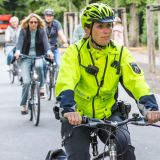 Eine Polizistin auf dem Fahrrad fährt einer Gruppe fahrradfahrender Menschen voraus