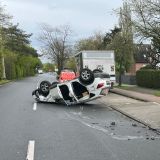 Weißer Nissan liegt verbeult auf seinem Dach auf der Straße