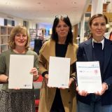 Eine Gruppe von fünf Personen, ein Mann und vier Frauen, steht in der Stadtbücherei zwischen Bücherregalen und hält Urkunden in den Händen