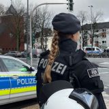 Eine uniformierte Polizistin der Einsazhundertschaft steht an einer Straßenkreuzung neben einem Streifenwagen