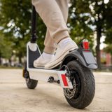 Eine Person in beigefarbener Jogginghose und weißen Sneakern fährt auf einem weißen E-Scooter.