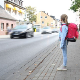 Mädchen mit Schultasche steht an befahrener Straße