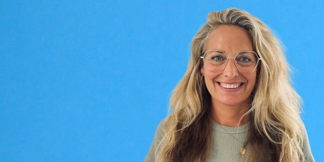 Blonde Frau mit Brille und hellgrünem T-Shirt strahlt in die Kamera