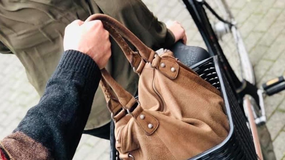 Eine Hand entwendet eine Handtasche aus einem Fahrradkorb