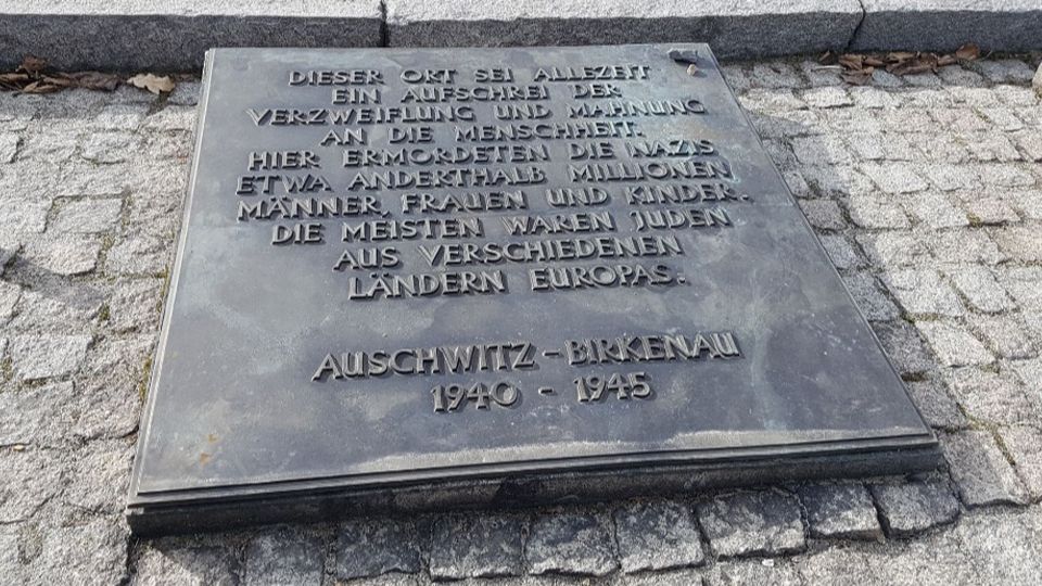 Eine graue Steinplatte mit einer Gedenkschrift darauf; fotografiert in Auschwitz