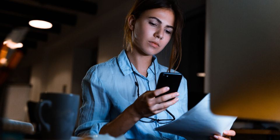 Eine junge Frau an ihrem Arbeitsplatz schaut auf ihr Smartphone